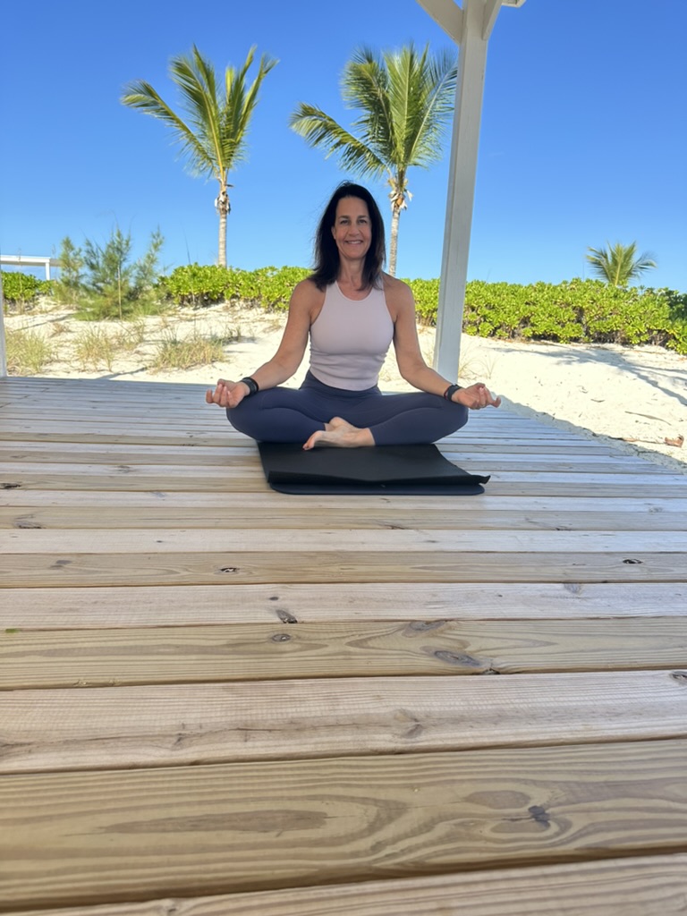 Marni meditating in lotus pose on a beach deck